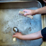 alt="a boy washing utensils in kitchen sink"