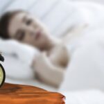 alt="a woman sleeping with a clock near her bed"