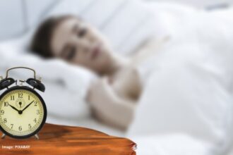 alt="a woman sleeping with a clock near her bed"